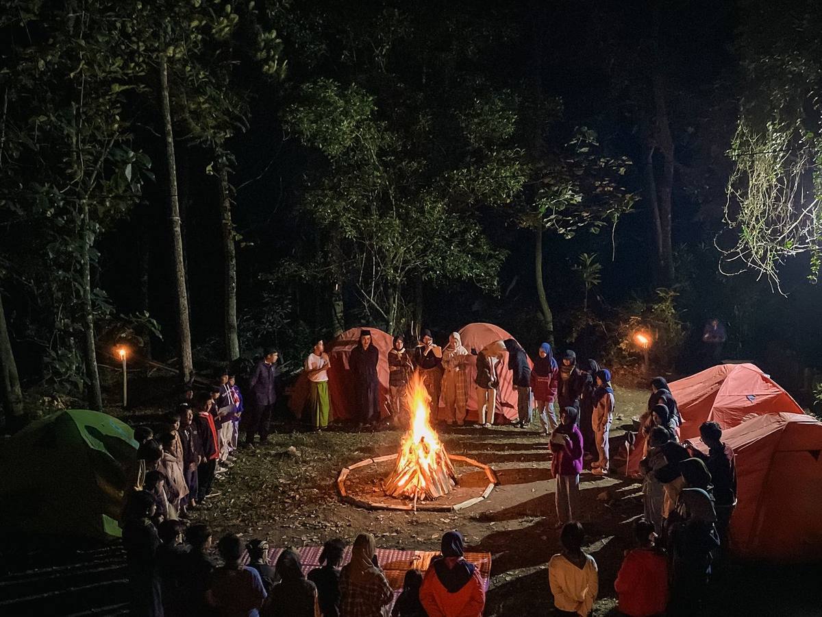 Malam perkemahan di hutan, berkumpul mengelilingi api unggun.